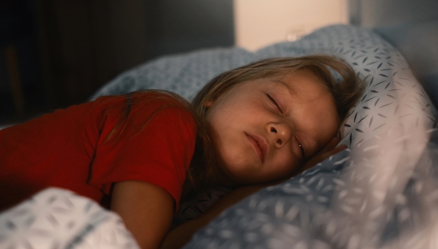 Child sleeping in bed at late night. Cute toddler girl pillow covered with warm blanket. Kid having night rest. Light on night table