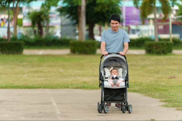 happy father pushing infant baby stroller and walking in the park