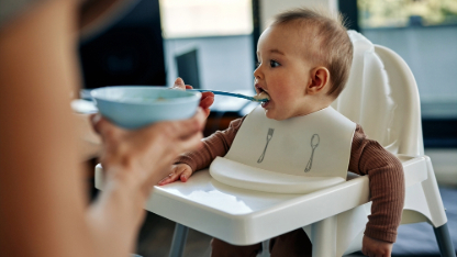 Unrecognized woman feeding her baby son sitting in a high chair.