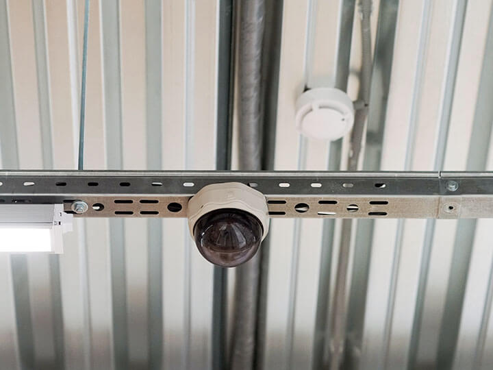 Security camera and smoke detector hanging on a metal interior ceiling